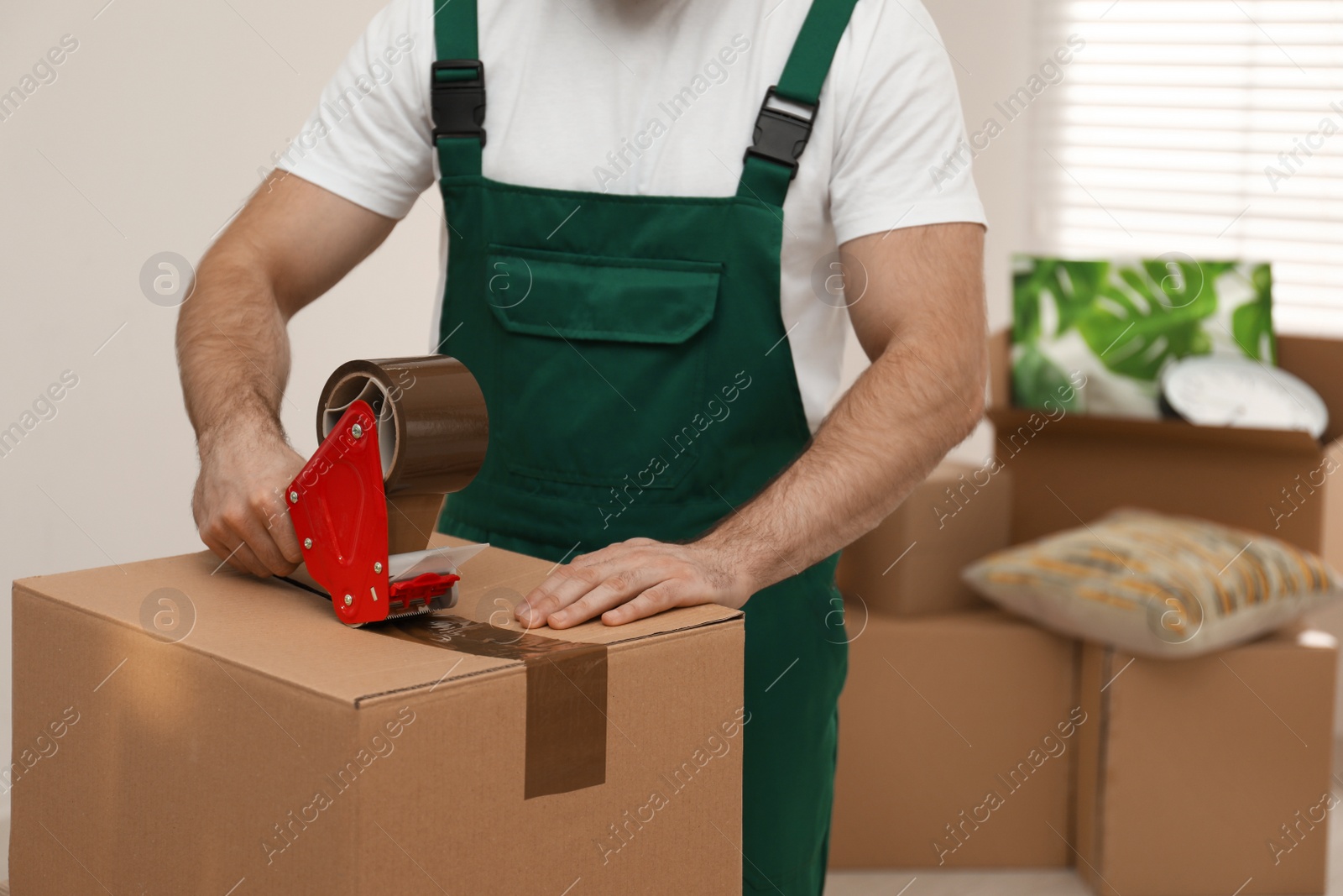 Photo of Man packing box with adhesive tape indoors, closeup. Moving service