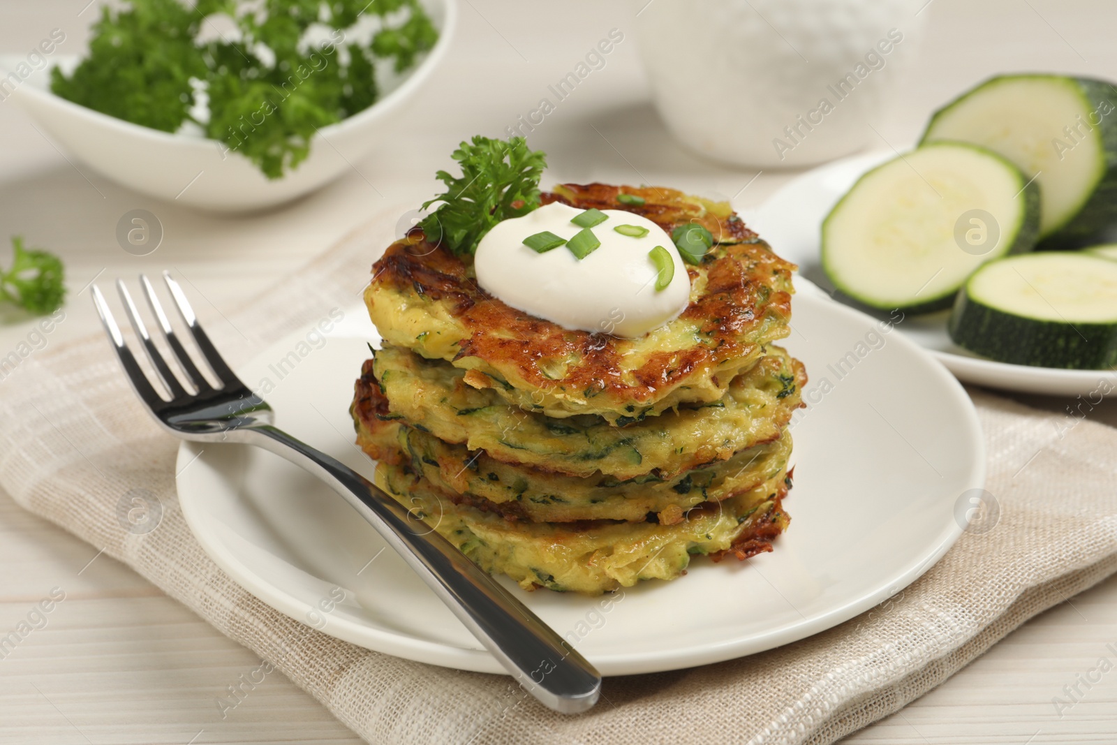 Photo of Delicious zucchini fritters with sour cream served on white wooden table