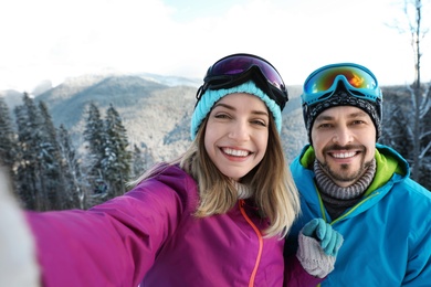 Happy couple taking selfie during winter vacation in mountains