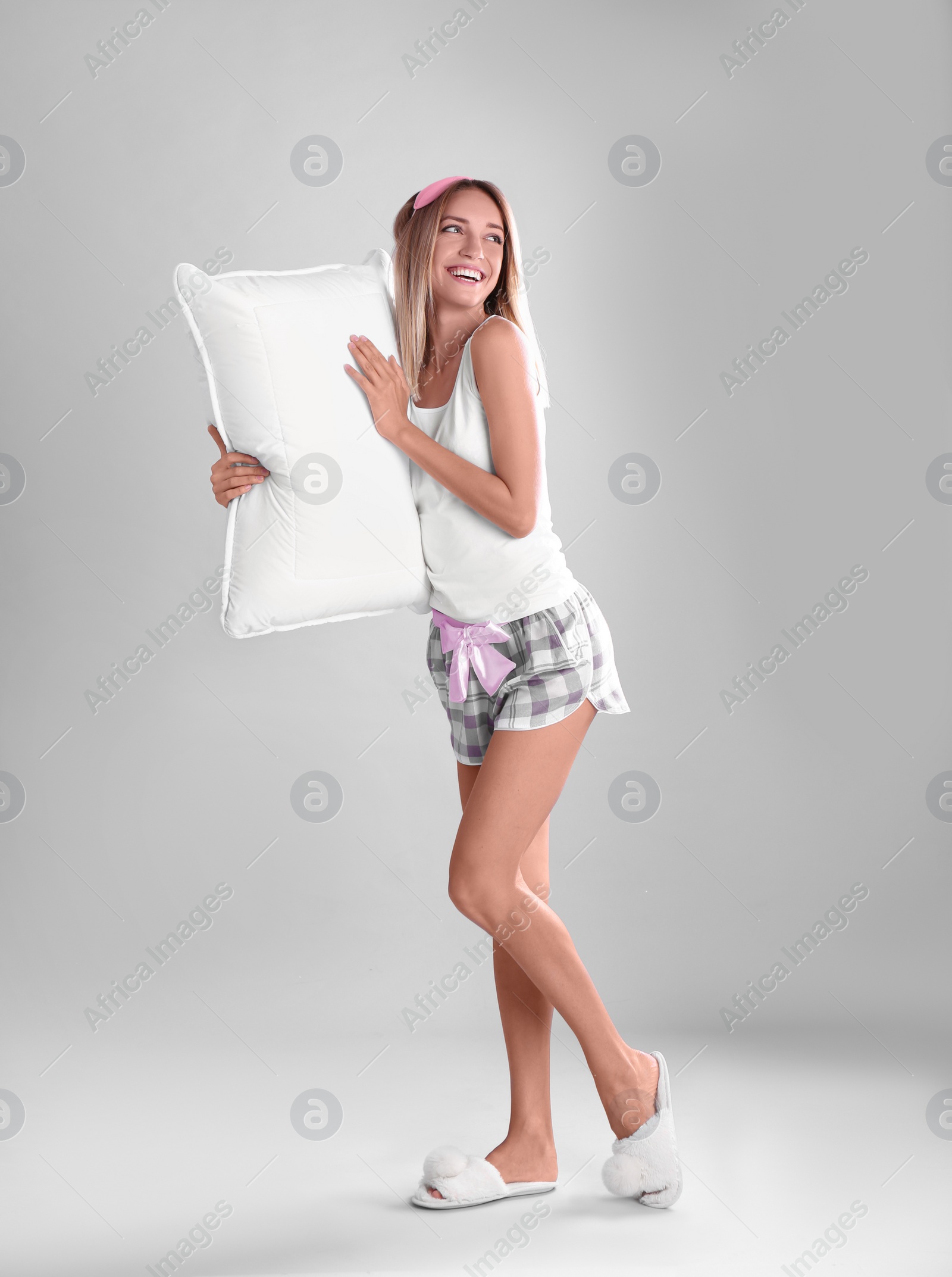 Photo of Happy woman in pajamas with pillow on gray background