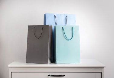 Photo of Paper shopping bags on white chest of drawers against light background