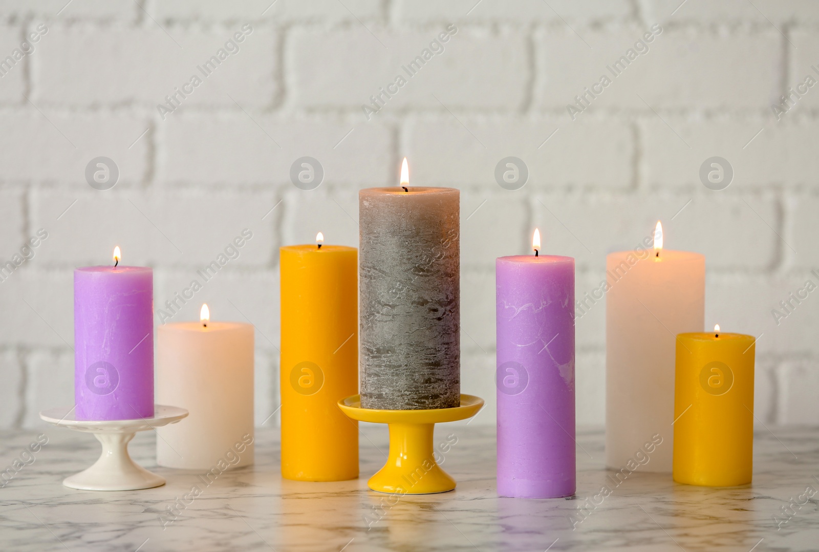 Photo of Different decorative wax candles on table against brick wall