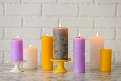 Photo of Different decorative wax candles on table against brick wall