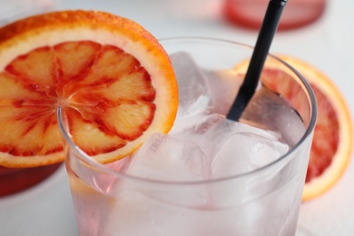 Glass of drink with ice cubes and orange, closeup