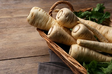 Photo of Wicker basket with delicious fresh ripe parsnips on wooden table, closeup
