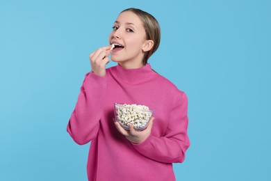 Teenage girl eating delicious popcorn on light blue background