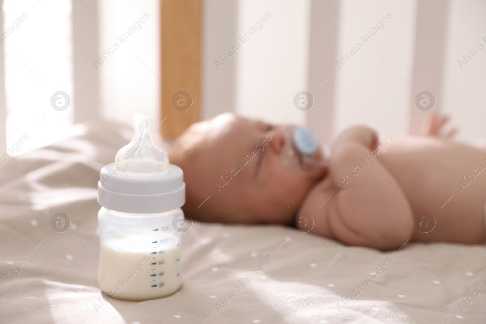 Photo of Healthy baby sleeping in cot, focus on bottle with milk