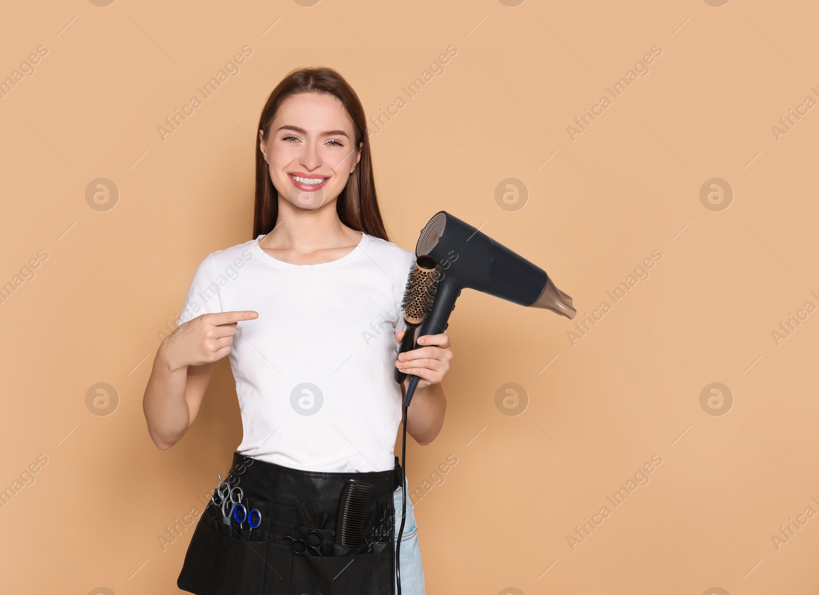 Photo of Portrait of happy hairdresser with hairdryer and brush on beige background. Space for text