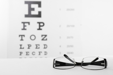 Photo of Glasses with corrective lenses on table against eye chart
