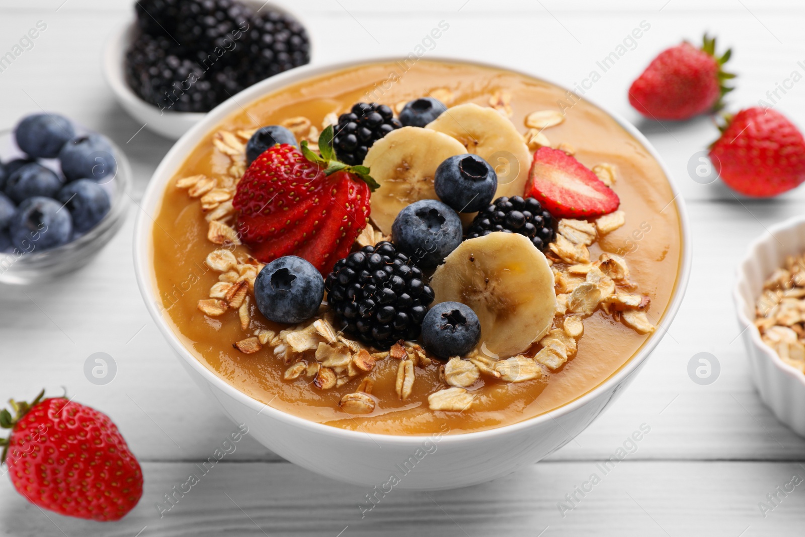 Photo of Delicious smoothie bowl with fresh berries, banana and oatmeal on white wooden table, closeup