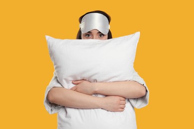 Tired young woman with sleep mask and pillow on yellow background. Insomnia problem