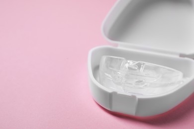 Photo of Bite correction. Container with dental mouth guard on pink background, closeup. Space for text