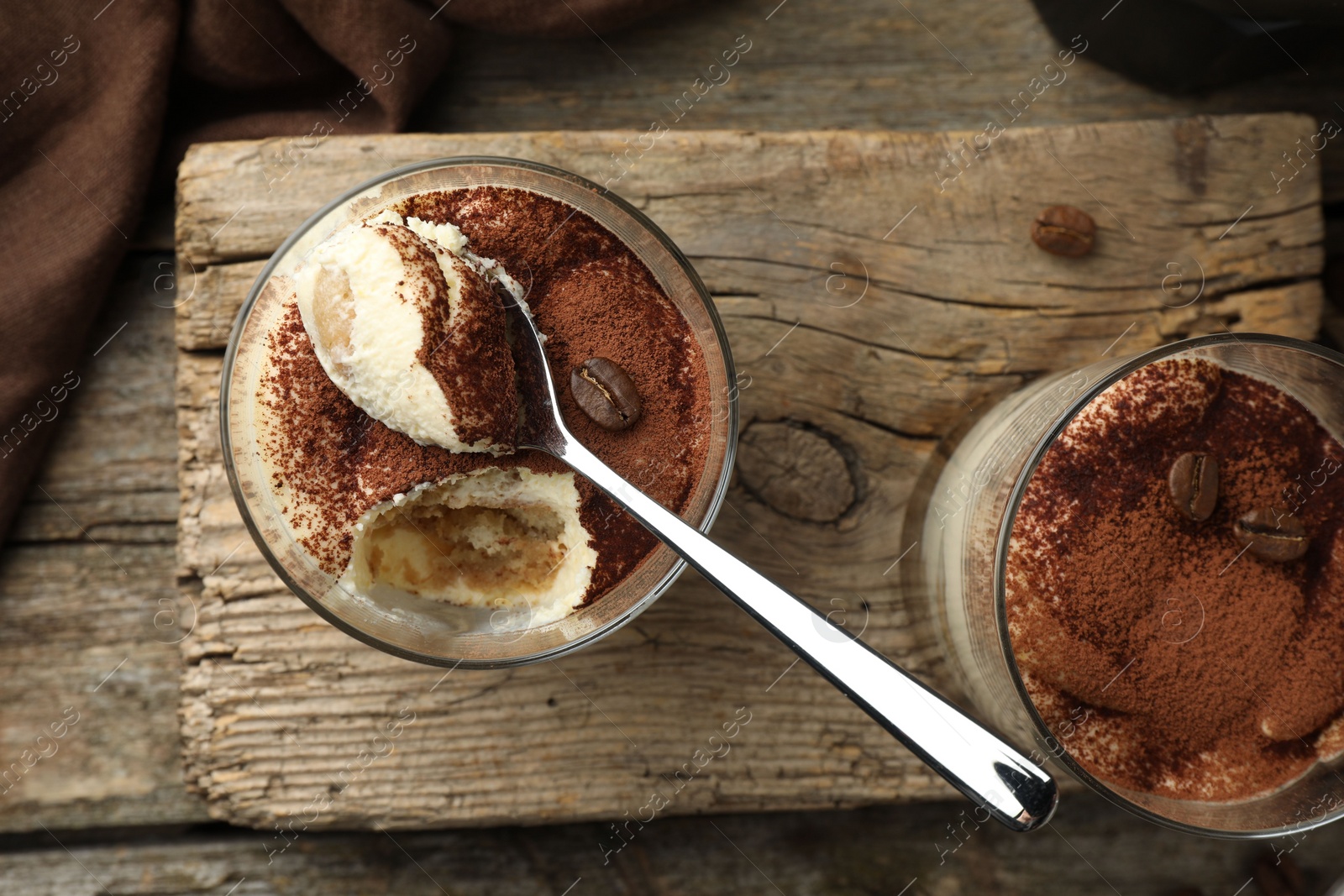 Photo of Delicious tiramisu in glasses, spoon and coffee beans on wooden table, top view