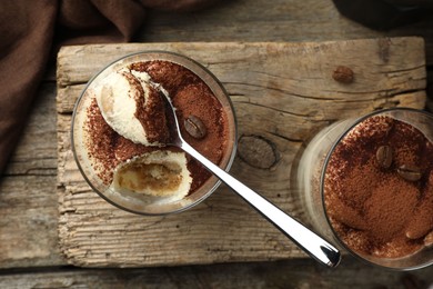 Delicious tiramisu in glasses, spoon and coffee beans on wooden table, top view