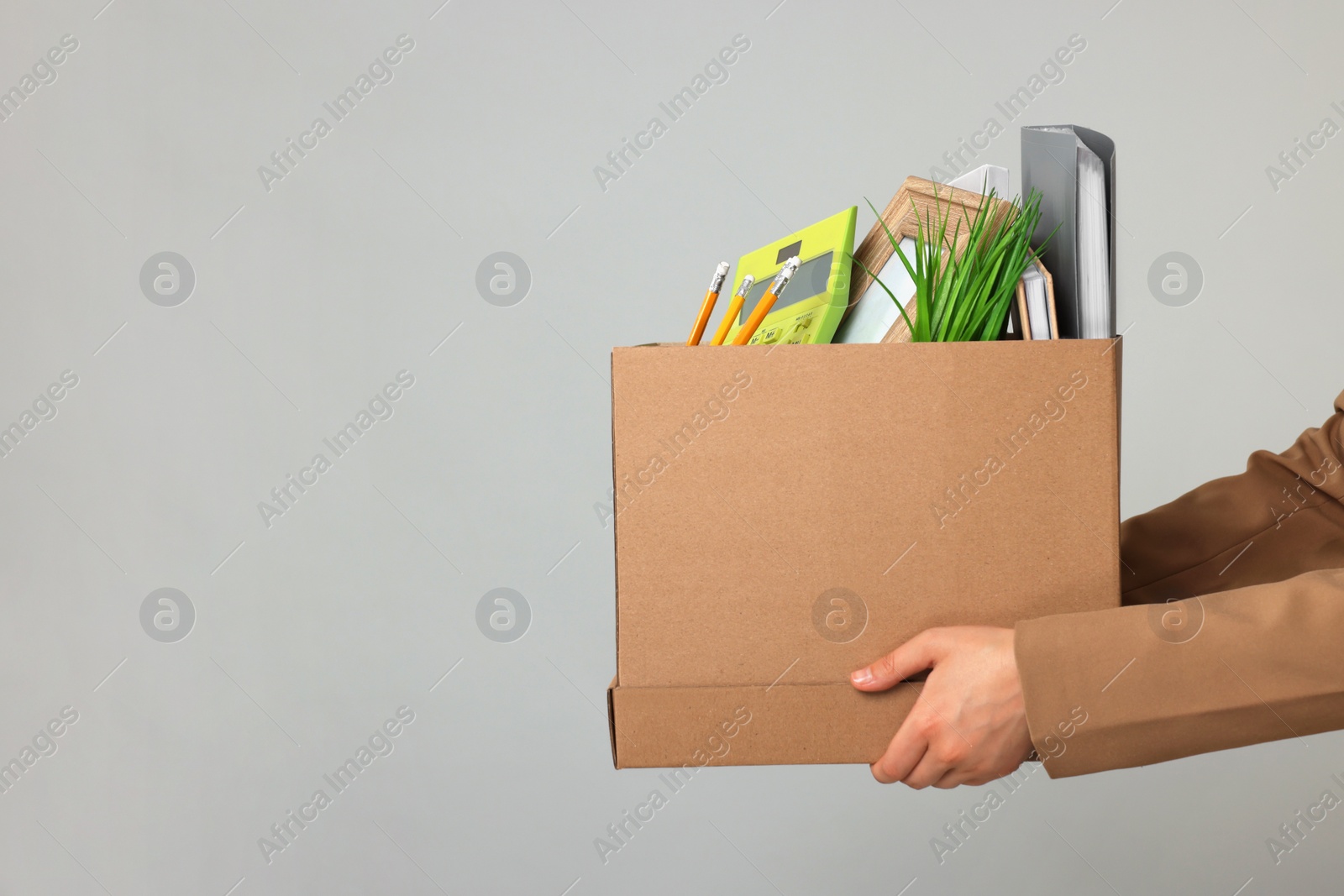 Photo of Unemployed woman holding box with personal office belongings on grey background, closeup. Space for text