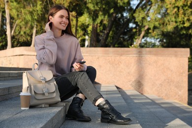Photo of Young woman with smartphone and stylish beige backpack on stairs outdoors, space for text