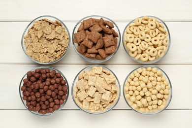 Different breakfast cereals in glass bowls on white wooden table, flat lay