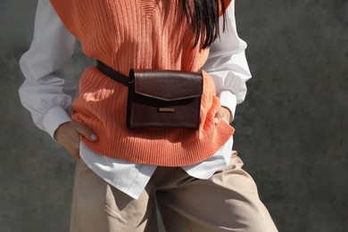 Photo of Young woman with stylish waist bag near grey wall outdoors, closeup