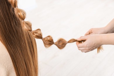 Photo of Professional stylist braiding woman's hair on blurred background, closeup