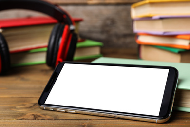 Photo of Modern smartphone with blank screen and books on wooden table, closeup. Space for design