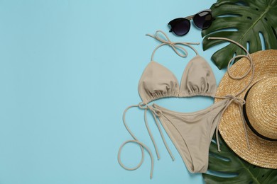 Photo of Stylish bikini, straw hat, sunglasses and tropical leaves on light blue background, flat lay. Space for text