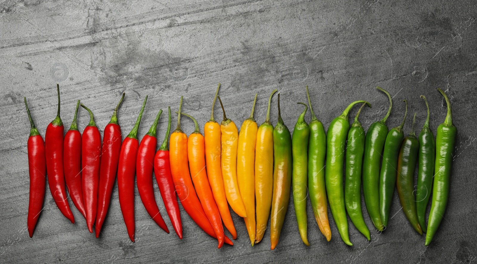Photo of Different ripe chili peppers grey table, flat lay. Space for text