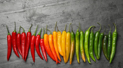 Photo of Different ripe chili peppers grey table, flat lay. Space for text