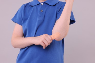 Little boy putting sticking plaster onto elbow against light grey background, closeup