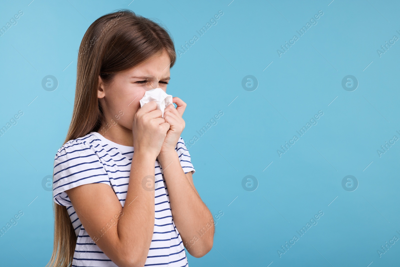 Photo of Sick girl with tissue coughing on light blue background, space for text