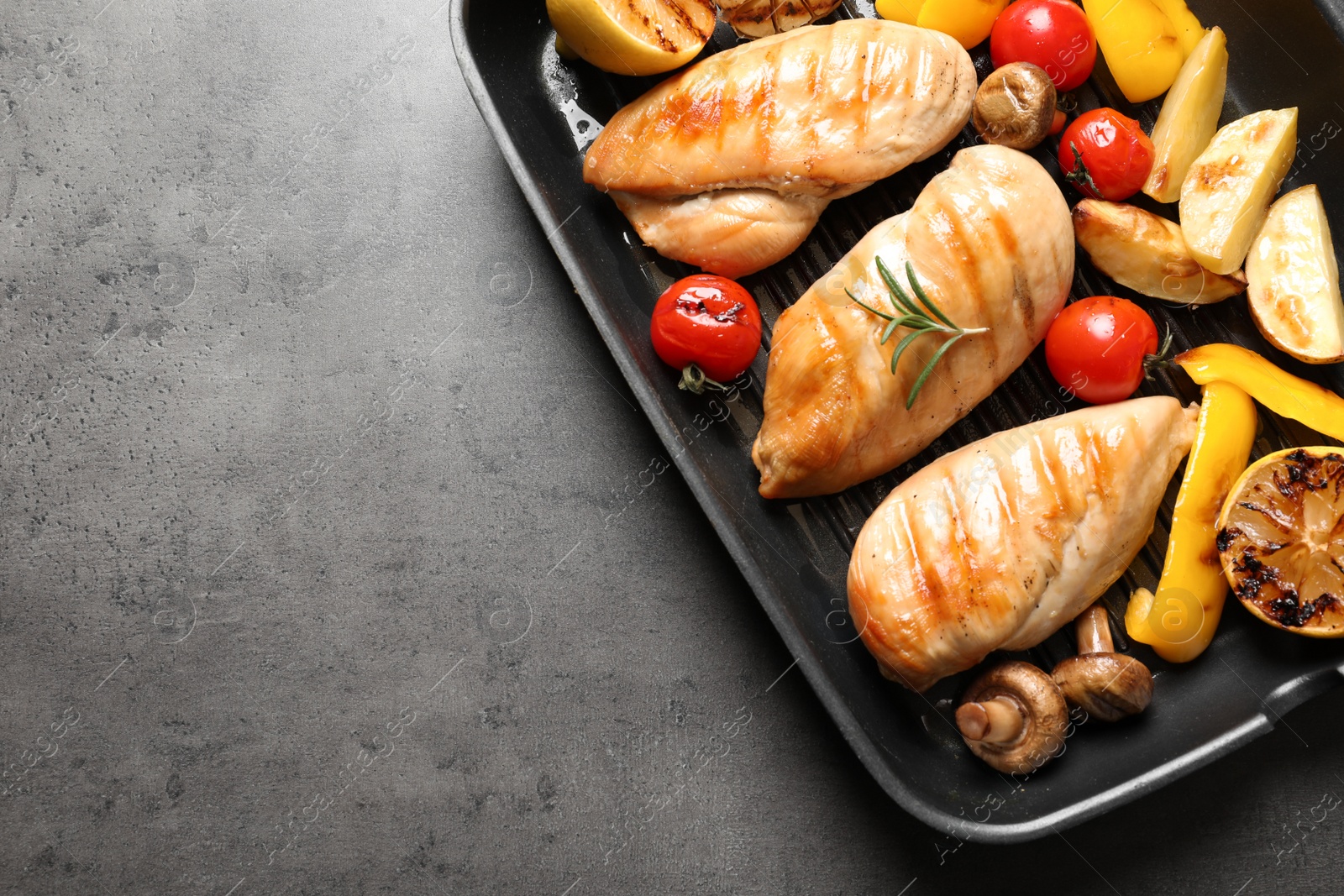 Photo of Grill pan with fried chicken breasts and garnish on grey background, top view. Space for text