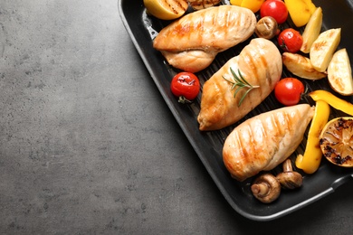 Grill pan with fried chicken breasts and garnish on grey background, top view. Space for text