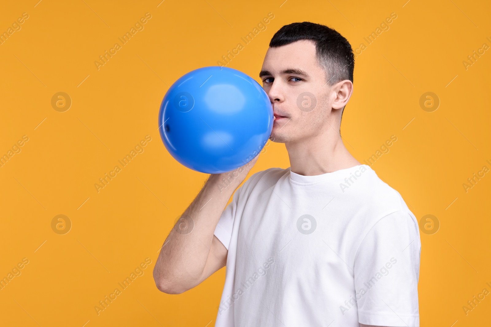 Photo of Young man inflating light blue balloon on yellow background