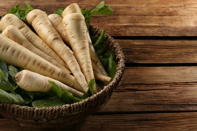 Photo of Fresh ripe parsnips in wicker basket on wooden table. Space for text