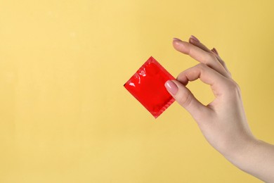 Photo of Woman holding condom on pale yellow background, closeup. Space for text