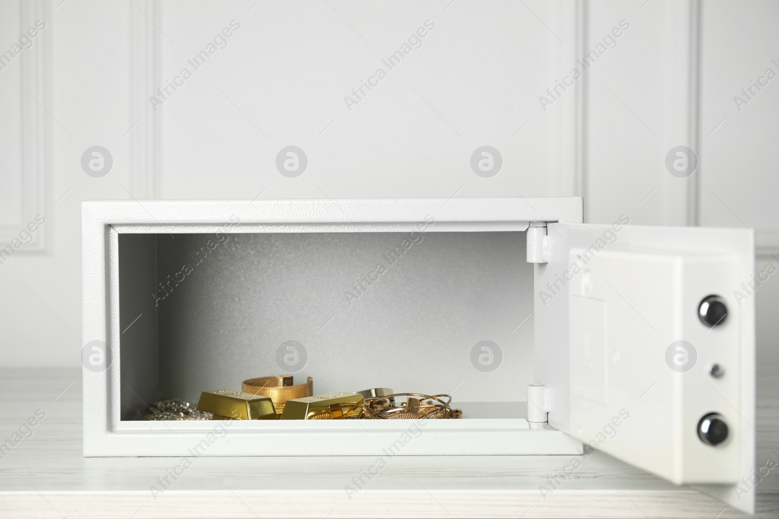 Photo of Open steel safe with gold bars and jewelry on wooden table
