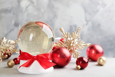 Photo of Beautiful snow globe and Christmas balls on light table. Space for text