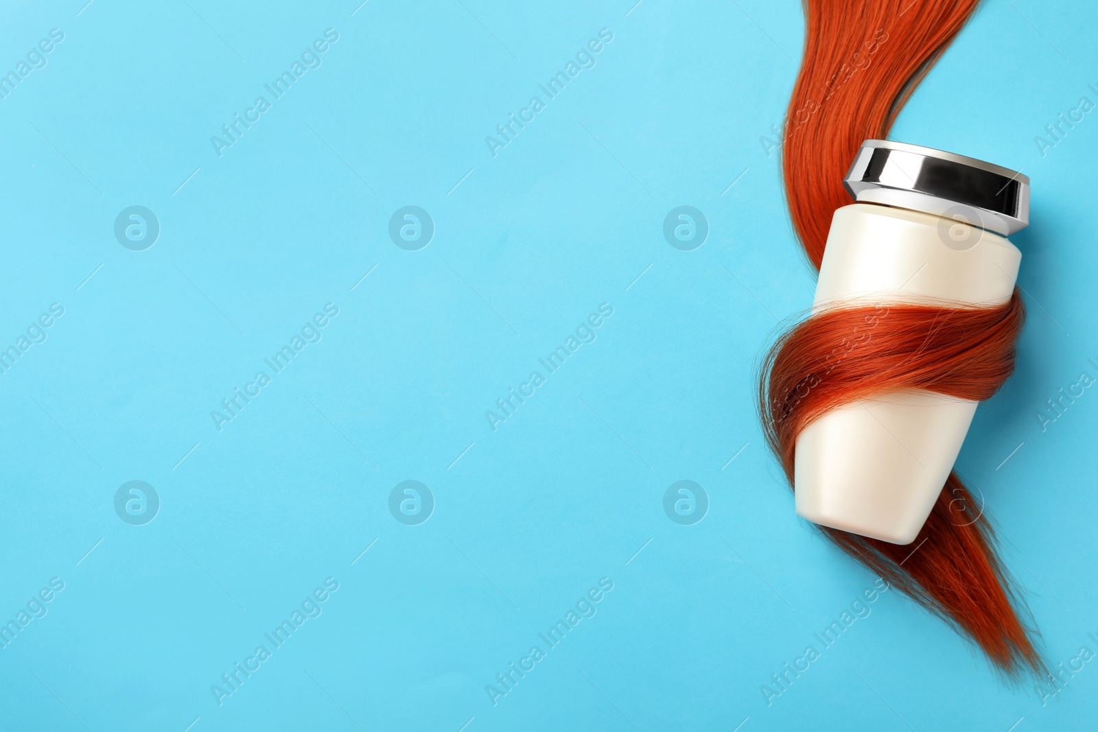 Photo of Bottle wrapped in lock of hair on light blue background, top view with space for text. Natural cosmetic product