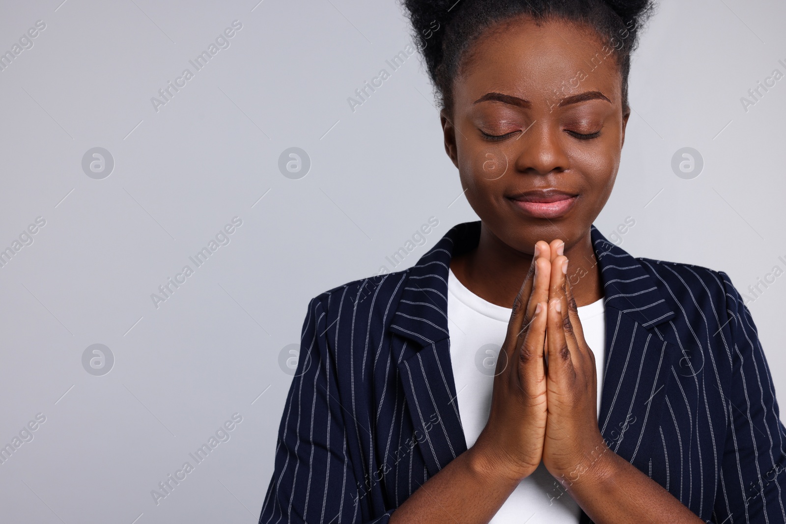 Photo of Woman with clasped hands praying to God on light grey background. Space for text