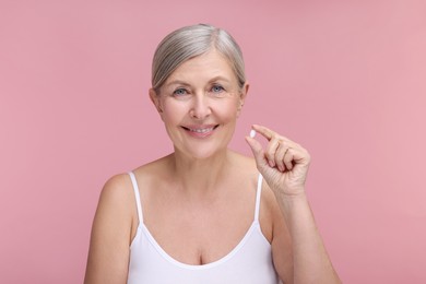 Beautiful woman with vitamin pill on pink background