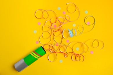 Photo of Beautiful serpentine and confetti bursting out of party popper on yellow background, flat lay