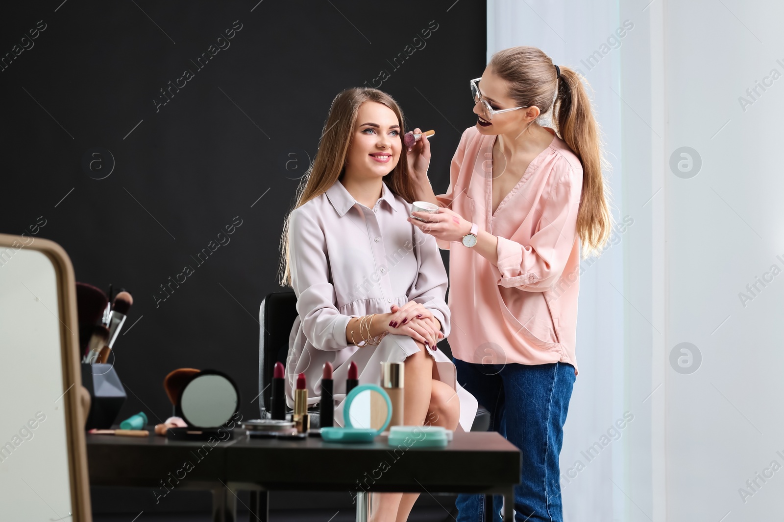 Photo of Professional makeup artist working with beautiful young woman in photo studio