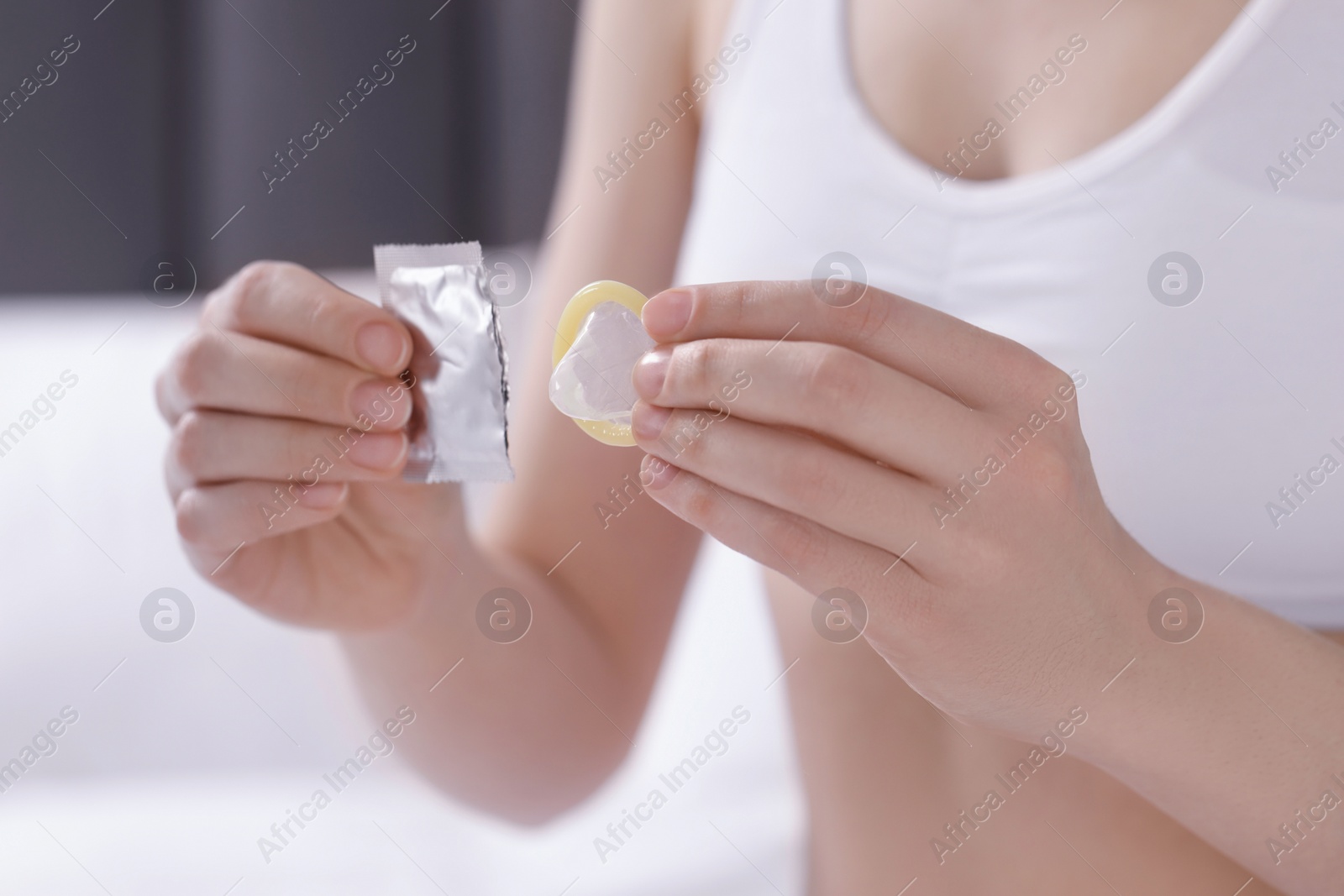 Photo of Woman holding unwrapped condom indoors, closeup. Safe sex