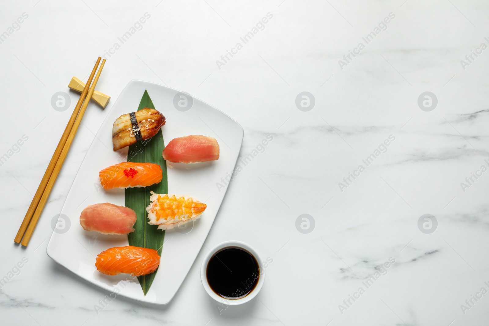 Photo of Plate with delicious nigiri sushi, chopsticks and soy sauce on white marble table, flat lay. Space for text