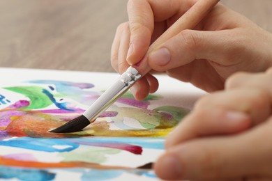 Photo of Woman painting with watercolor at wooden table, closeup