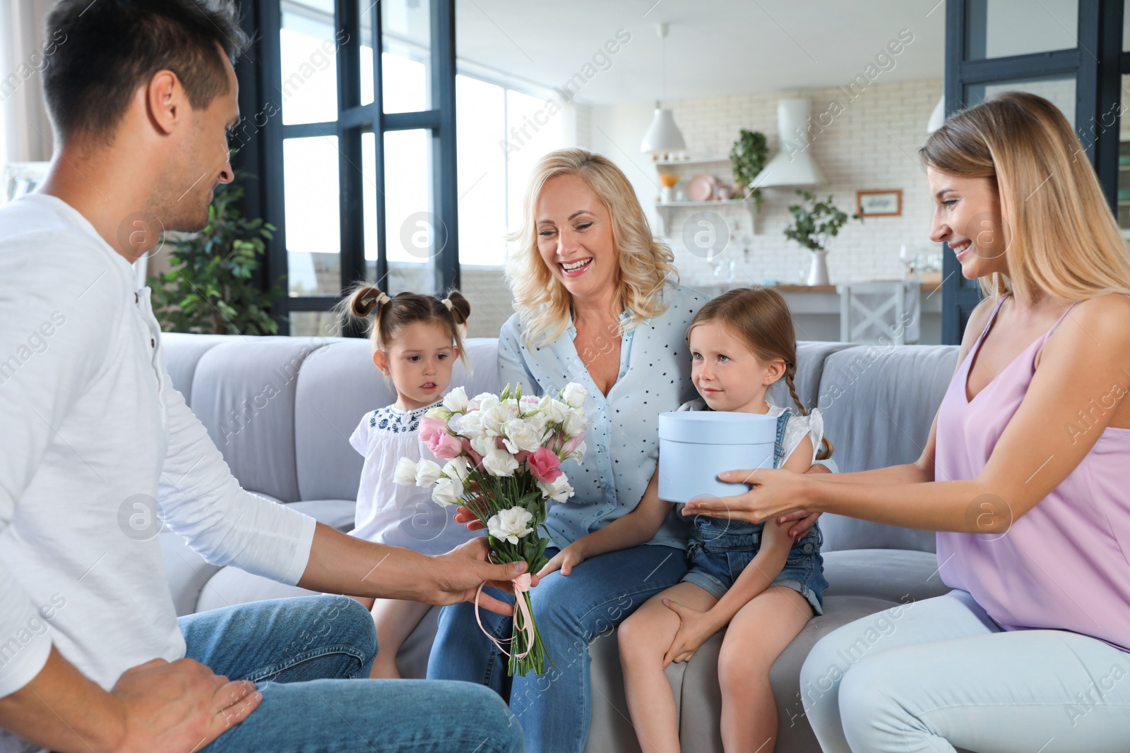 Photo of Happy family with little children congratulating mature woman in living room