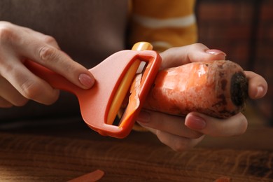 Woman peeling fresh carrot at table indoors, closeup