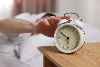 Photo of Man turning off alarm clock in bedroom, focus on hand