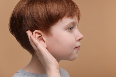 Photo of Little boy with hearing problem on pale brown background, closeup