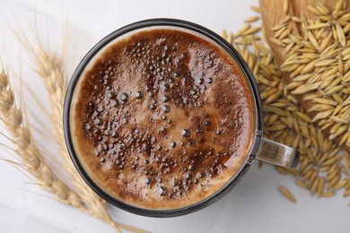 Photo of Cup of barley coffee, grains and spikes on white table, flat lay