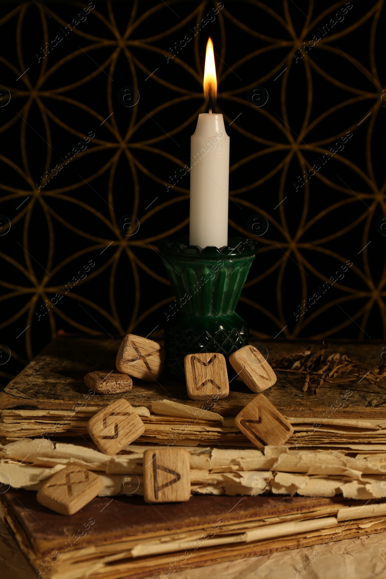 Photo of Wooden runes and burning candle on old books